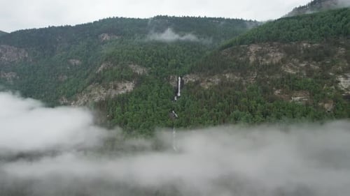 Aerial video flying between clouds over a waterfall. Norway