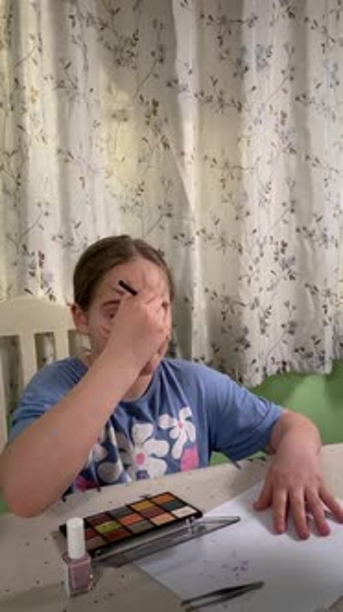 Young Girl Paints Face with Makeup at Table