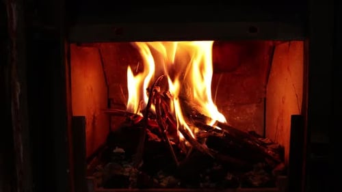 A wooden fire burning in a small fireplace with big flames and sparks. 4k shot.