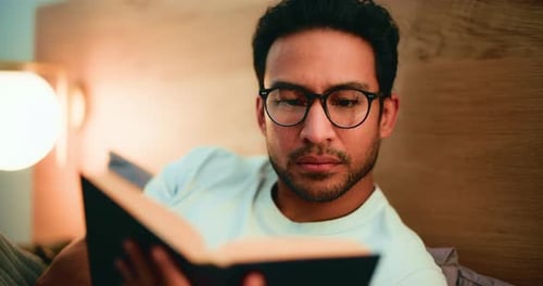 Man Reading Book in Bed Under Warm Light