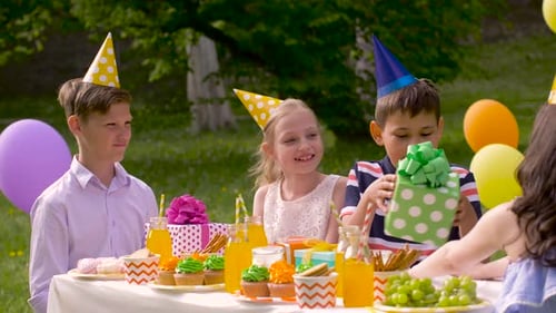 Happy kids celebrate birthday party with gifts and sweets in summer garden
