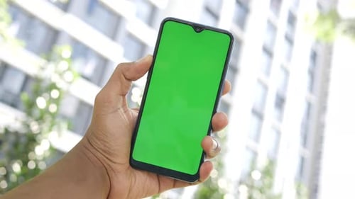 Young Man Hand Using Smart Phone with Green Screen Against City Buildings