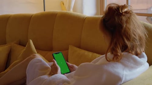 Vertical green screen phone held by woman sitting on couch home alone.