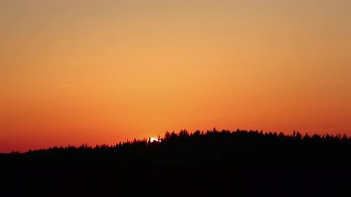 Timelapse shot of golden sunset along colorful sky behind tree silhouette during evening time.