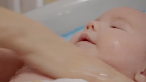 Close up hand of mother bubble bathing the body of her son in warm water.