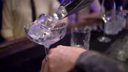 Bartender Adds Ice to Coupe Glass at Night