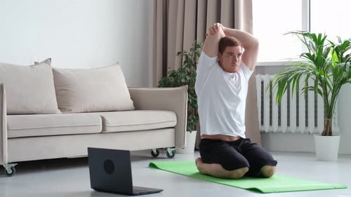 Redhead Man in White Tshirt Works Out in the Living Room Man Doing Sports on a Mat Watching Videos