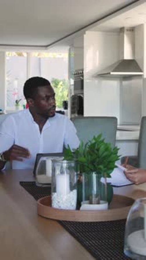 Vertical video: African American man gesturing at dining table glancing tablet before sipping water