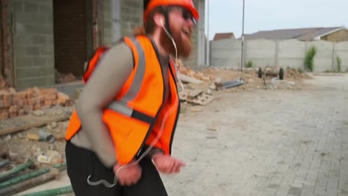 Um engenheiro arquitetônico barbudo e sorridente, com colete laranja e capacete, dança em um aniversário