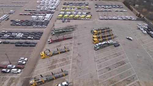 An aerial video of a car depot showcasing rows of parked cars, vans, and yellow commercial vehicles.