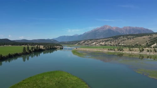 Scenic River Valley With Lush Meadows, Trees, and Majestic Mountains Under a Clear Blue Sky