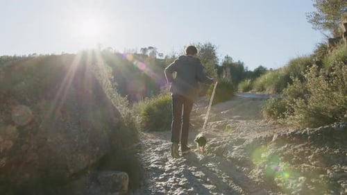 Hiker Traversing Leashed Trail with Small Dog Rocky Terrain Backlit By Golden Morning Sunlight in