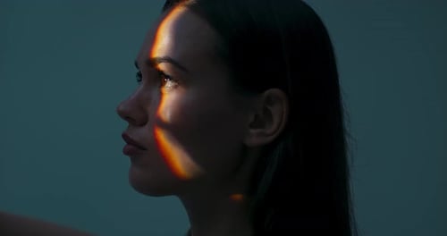 Jeune femme de profil debout en studio isolée dans une lumière vive regardant vers le haut en train de jouer avec la lumière