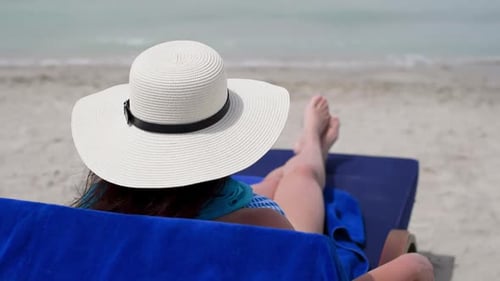 Woman Wearing Hat Resting on Deck Chair at Sandy Seashore on Beach