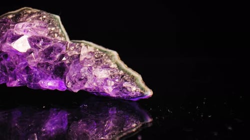Elegant macro pan of purple amethyst crystal lit against black background, with reflection below.
