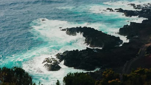 Slow motion wide shot of rocky coastline. Colorful turquoise ocean waves crushing on the rocks.