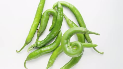green twisted hot pepper rotates on a white background with other peppers, top view