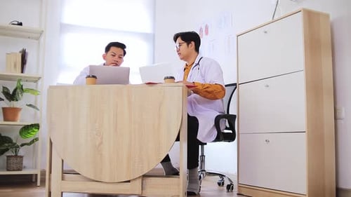 Two doctors collaborate discussing patient care using laptops in modern clinic office setting