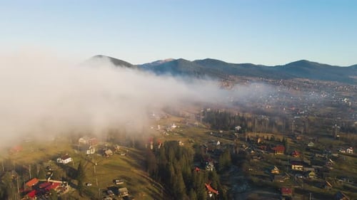 Aerial View of Vibrant Landscape of Foggy Clouds Covering Mountain Hills and Small Scattered Village