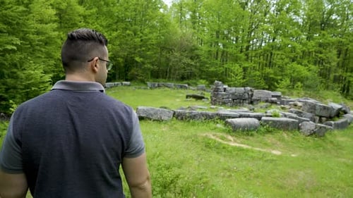 Man Walking Toward Ancient Ruins in Grassy Field