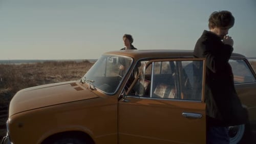 Couple Smoking by Vintage Car during Stop on Road Trip in Open Field