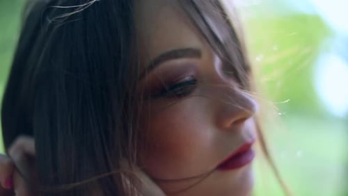 Beautiful Woman Putting on Earrings in Green Setting