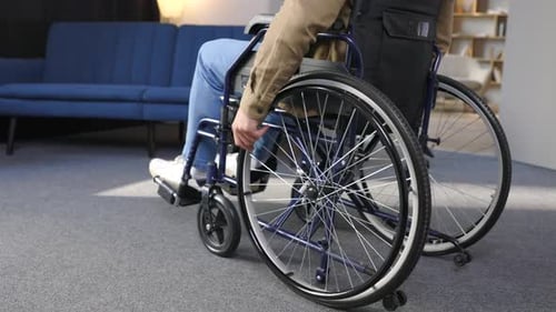 A disabled man is sitting in a wheelchair. He holds his hands on the wheel, close up