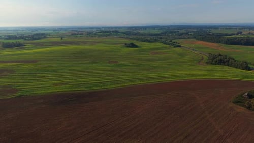 Aerial view of striped green and brown agricultural fields stretching into the horizon, showcasing