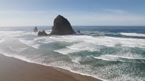 Blue water and crashing waves surround Haystack Rock at Cannon Beach