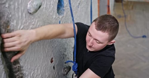 Man Climbing Indoor Rock Wall with Rope
