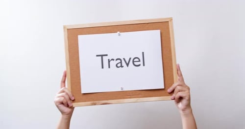 Woman's hand shows the paper on board with the word Travel in white studio background with copy spac
