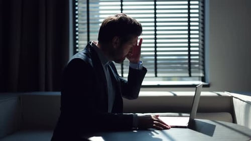 Frustrated Man Working on Laptop in Darkened Room
