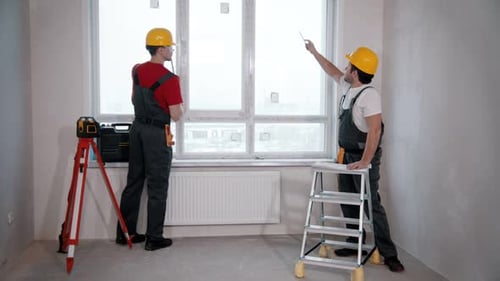 Wohnungsreparatur im Zimmer Zwei männliche Arbeiter messen die