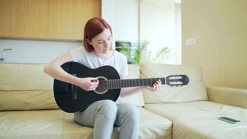 Woman Plays Guitar on Couch at Home