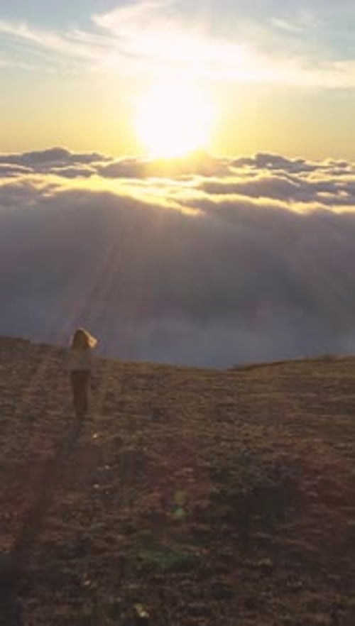 Woman is Walking to the Edge of Mountain Plateau Above Pink Clouds Vertical Video
