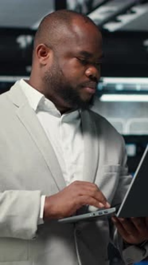 Vertical Video Technician Walking in Data Center Using Laptop to Check Hardware