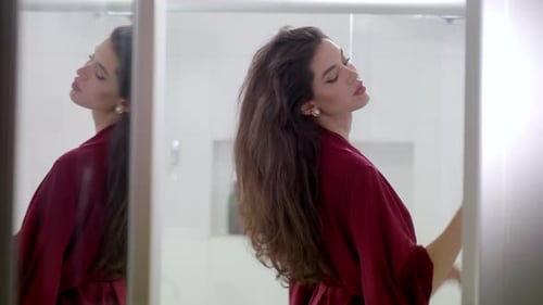 Glamorous Woman Styling Hair in Bathroom Mirror