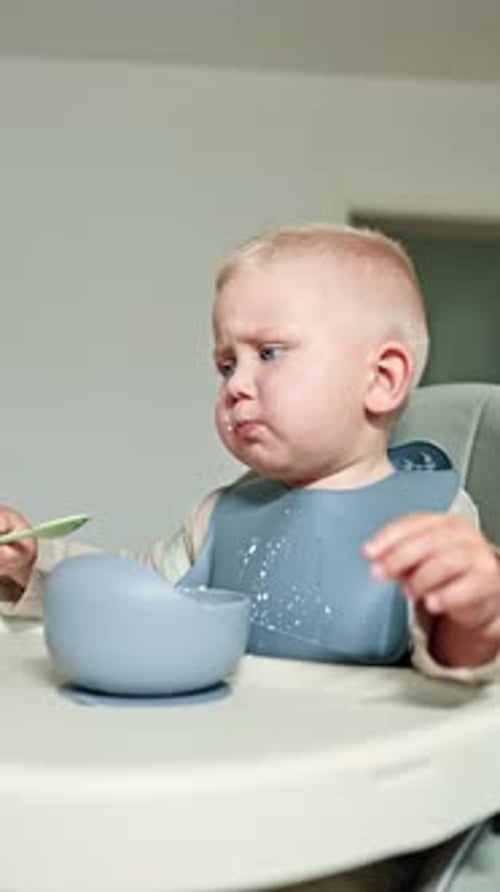 Cute Infant Eats from Bowl with Spoon