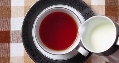 Adding Milk From a Jug to a Cup with Black Fragrant Tea Top Down View