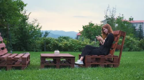 Beautiful Young Woman Enjoying the Sunset in Her Garden and Communicating on the Internet on a