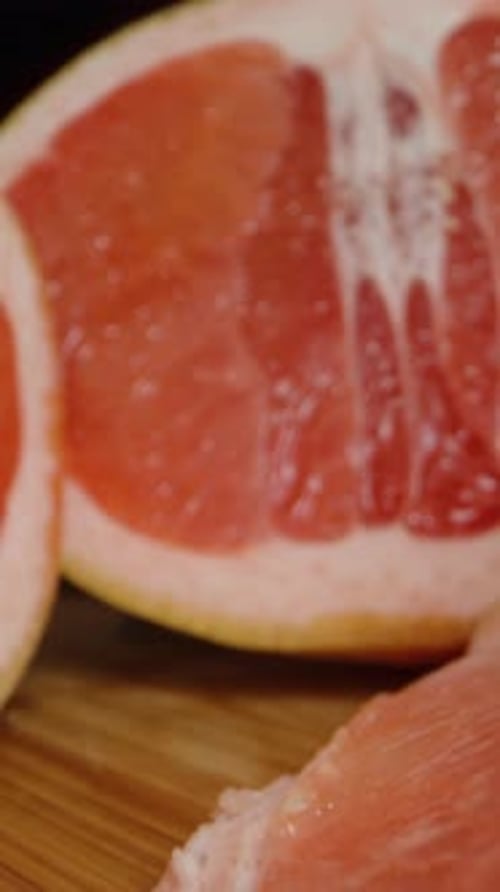 Vertical video. Sliced grapefruit on a wooden cutting board, the camera moves backward.