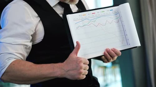 Unrecognized man in white shirt and black vest holding a piece of paper with graphs.
