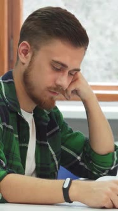 Man Looking Tired While Reading at Desk