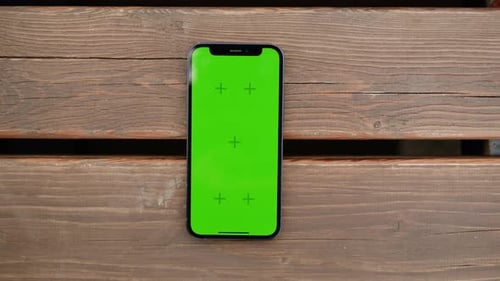 Telefon mit Chroma-Key-Bildschirm auf Holzhintergrund, Nahaufnahme, grüner Bildschirm auf Smartphone, Natur