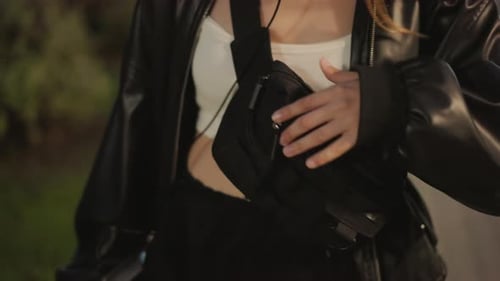 Woman Adjusting Sling Bag with Book While Walking Through Park at Twilight Leather Jacket Candid