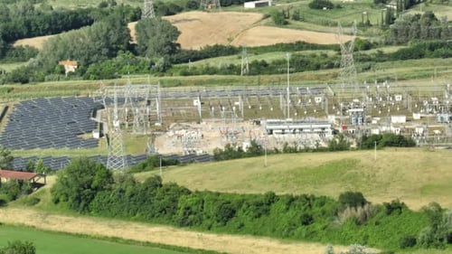 Photovoltaic Station With High-voltage Towers And Solar Panels In Italy. aerial shot