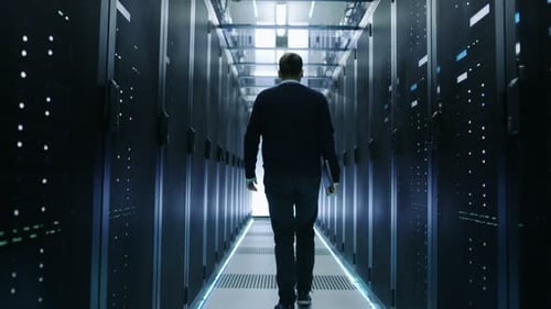 Vista posterior de un ingeniero de TI recorriendo un centro de datos con servidores en rack en funcionamiento.