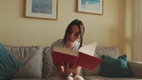 Junge Frau liest ein Buch und sitzt zu Hause auf dem Sofa