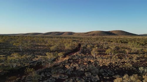 Aerial establishing shot of abandoned road in Australian desert during sunset time. Bush and plants