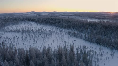 Aerial view following convoy of snowmobile through snow covered Scandinavian woodland wilderness tra